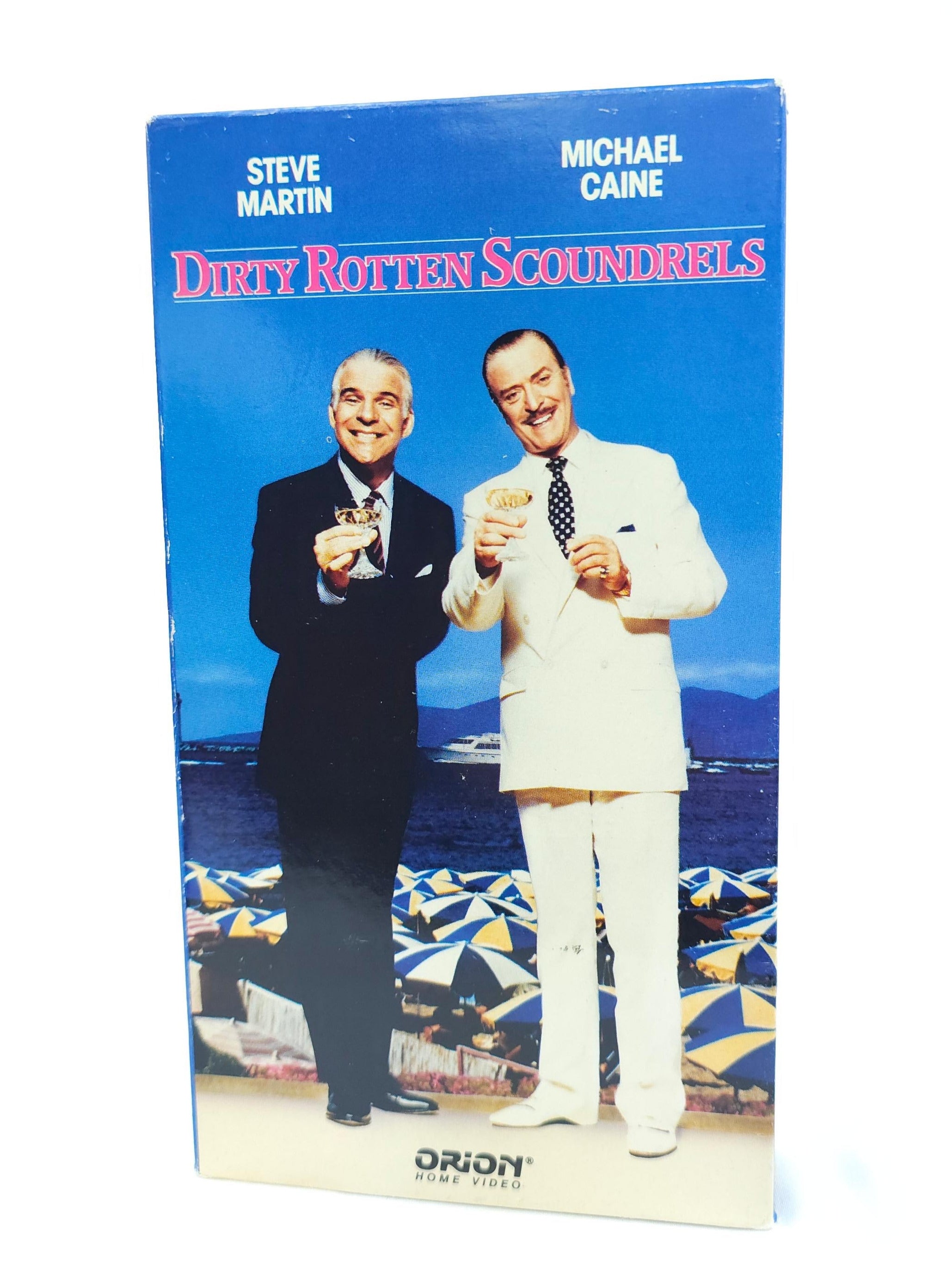 VHS cover of 'Dirty Rotten Scoundrels' with two men on a boat, featuring Steve Martin and Michael Caine.